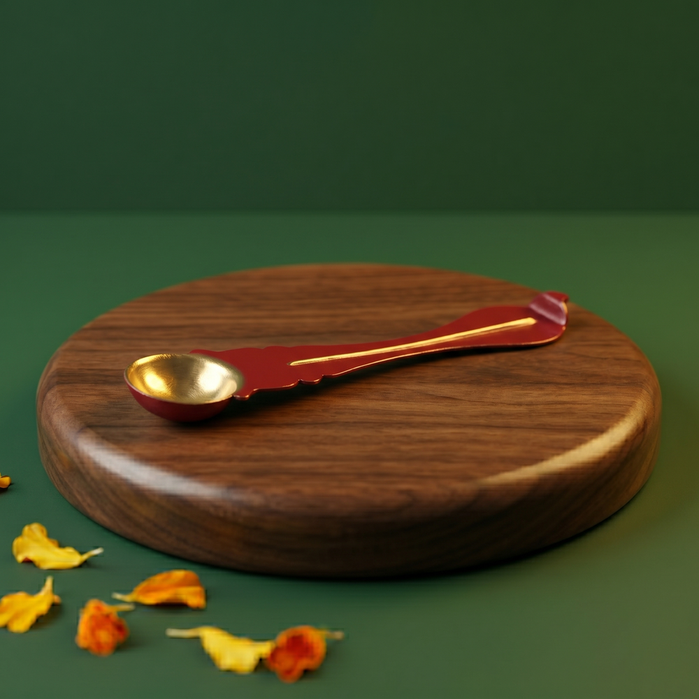 Brass Uthrani spoon with decorative handle in right side angle on wooden plate with scattered yellow and orange petals.