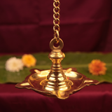 Thookku Vilakku hanging lamp with chain and scalloped base in close-up top-angle view with flowers on a banana leaf against a maroon backdrop