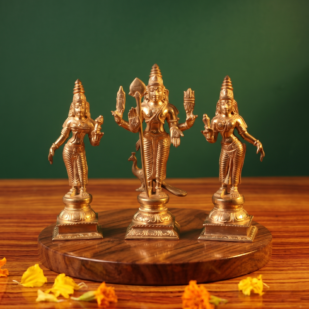 Panchalogam Murugan Set in front view with Valli and Devasena flanking him with a peacock at the base on a wooden plate against a green background.