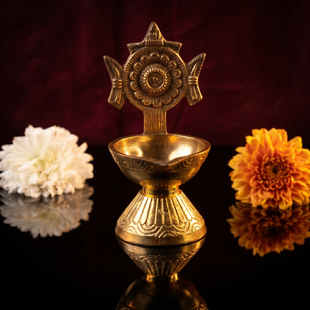 Sangu Chakaram Vilakku with floral chakra in front view with white and orange flowers on dark reflective surface against maroon backdrop