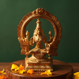 Lakshmi idol in front view with circular arch prabhavali seated on a lotus base with yellow and orange petals on wooden plate.