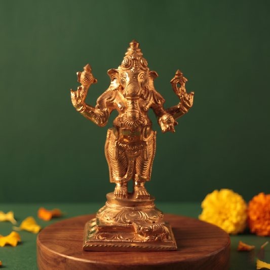 Ganesh Standing Valampuri in front view with four arms on an engraved base with yellow and orange marigolds on a wooden plate.