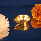 Agal Vilakku in a slight top-angle right-side view on a reflective blue surface with white and orange flowers against a blue backdrop