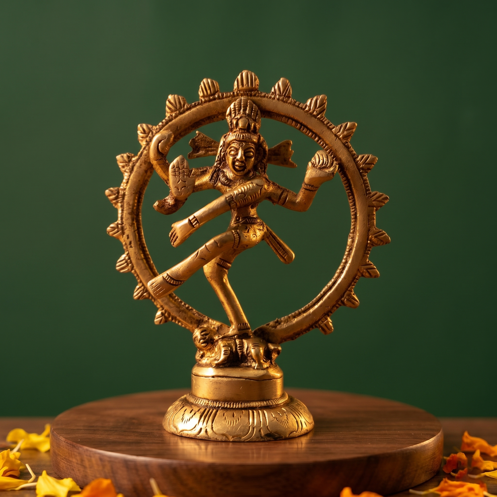 Brass Nataraja idol in a straight front-facing dancing pose within a fire ring, on a wooden platform with marigold petals, green backdrop.