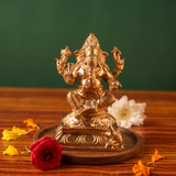Ganesh Sitting Edampuri in front view, seated on a lotus base with red and white flowers and scattered petals on a wooden plate.