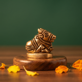 Brass Nandi idol in a slight left-angle resting pose on a round pedestal, on a wooden platform with marigold petals, green backdrop.