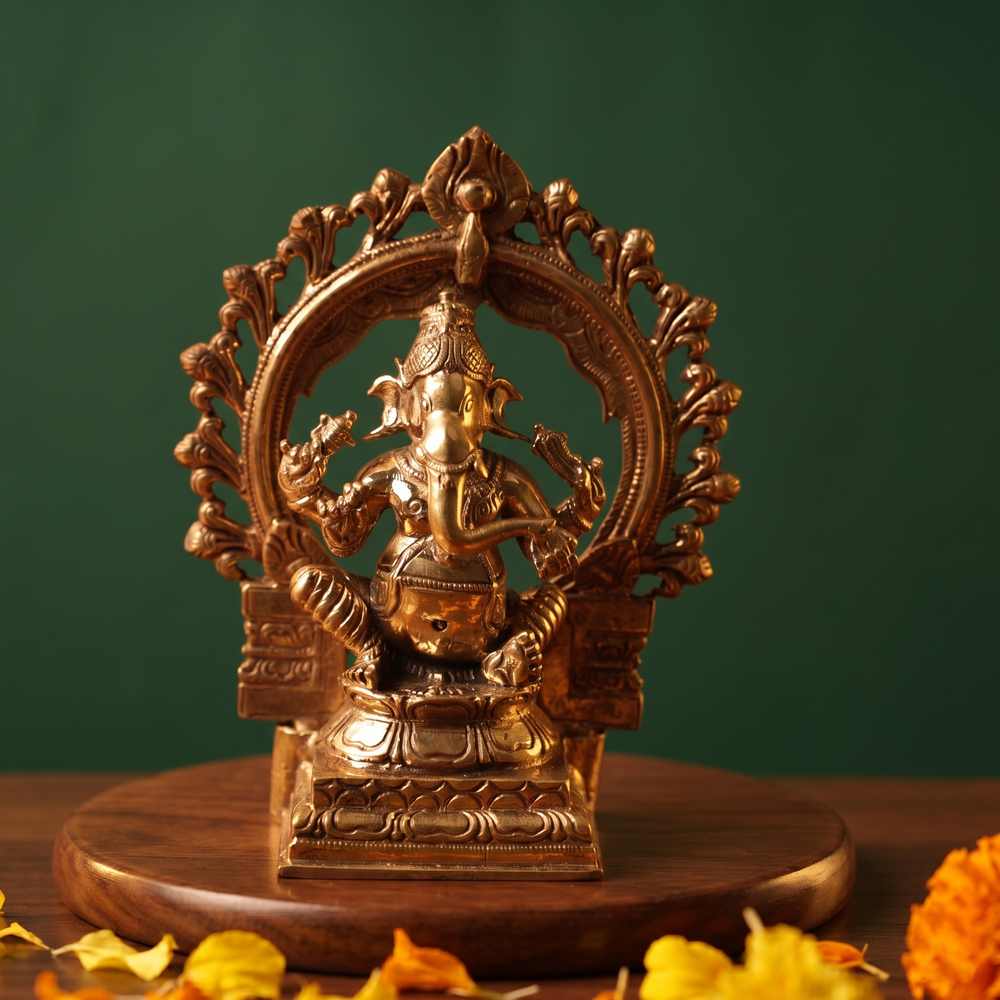 Ganesh Sitting Edampuri in front view with circular floral arch seated on a lotus base with yellow and orange marigolds on a wooden plate.