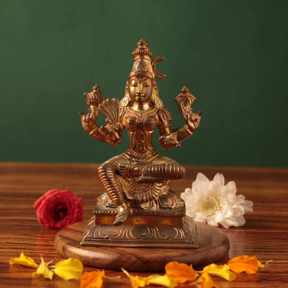 Raja Rajeshwari idol in front view, seated with four arms, with red and white flowers on a wooden plate.