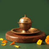Brass Kumkum Sindoor Box with domed lid on a brass plate in straight front view on a wooden base with marigold flowers on green surface