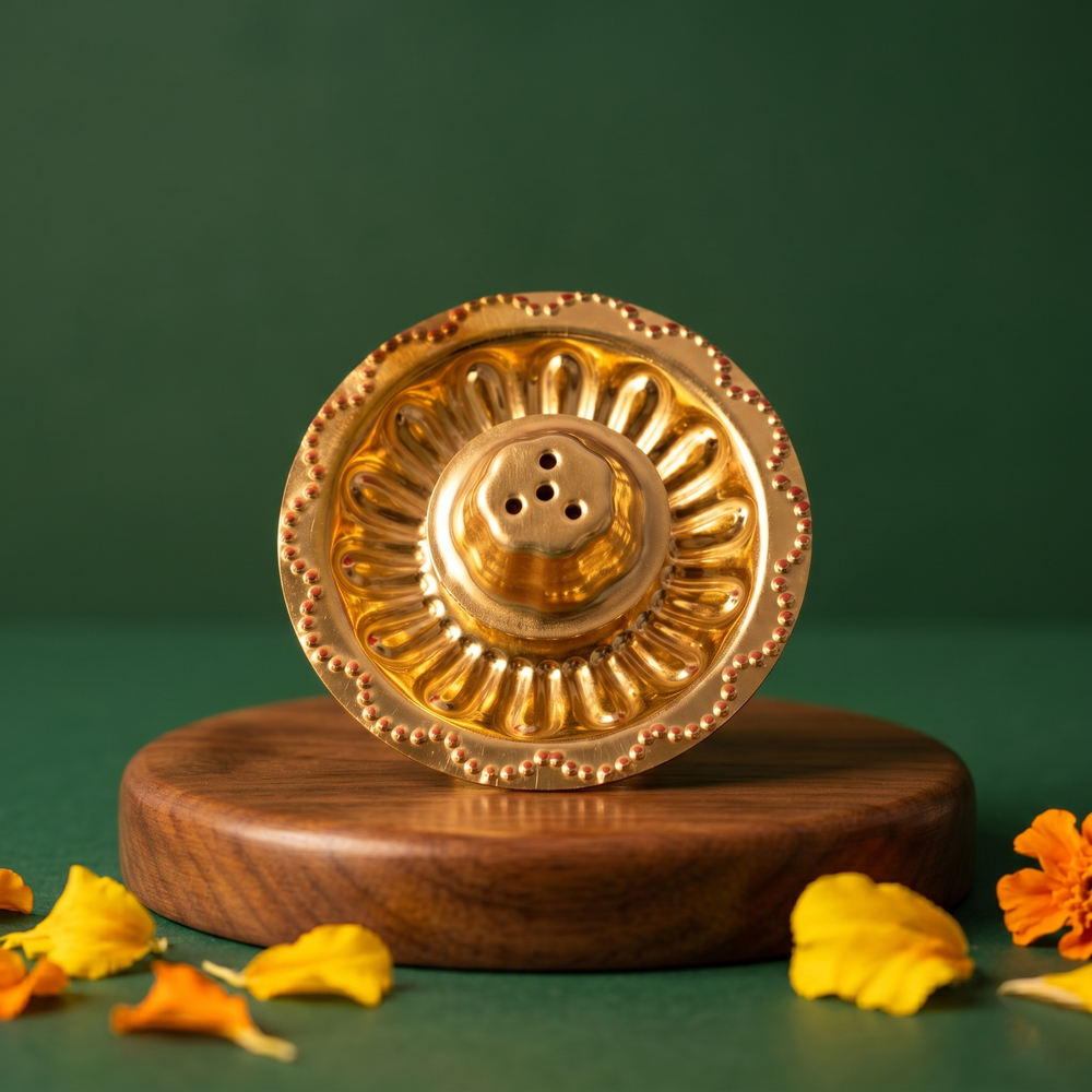 Brass Agarbatti Dhoop Stand top view showing circular floral design with incense holes, with scattered yellow and orange petals on a wooden plate.
