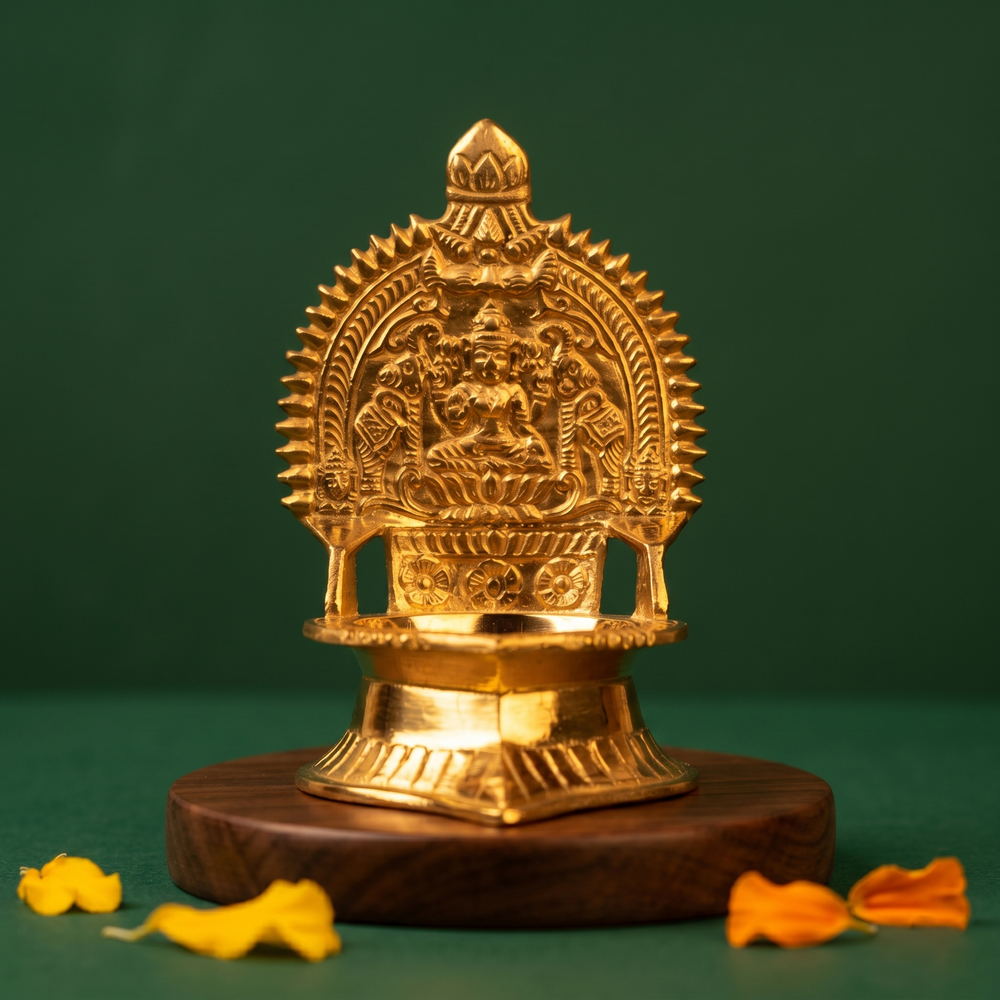Kamakshi Deepam Vilakku with goddess and prabhavali in straight front view on a wooden base with petals against a green backdrop