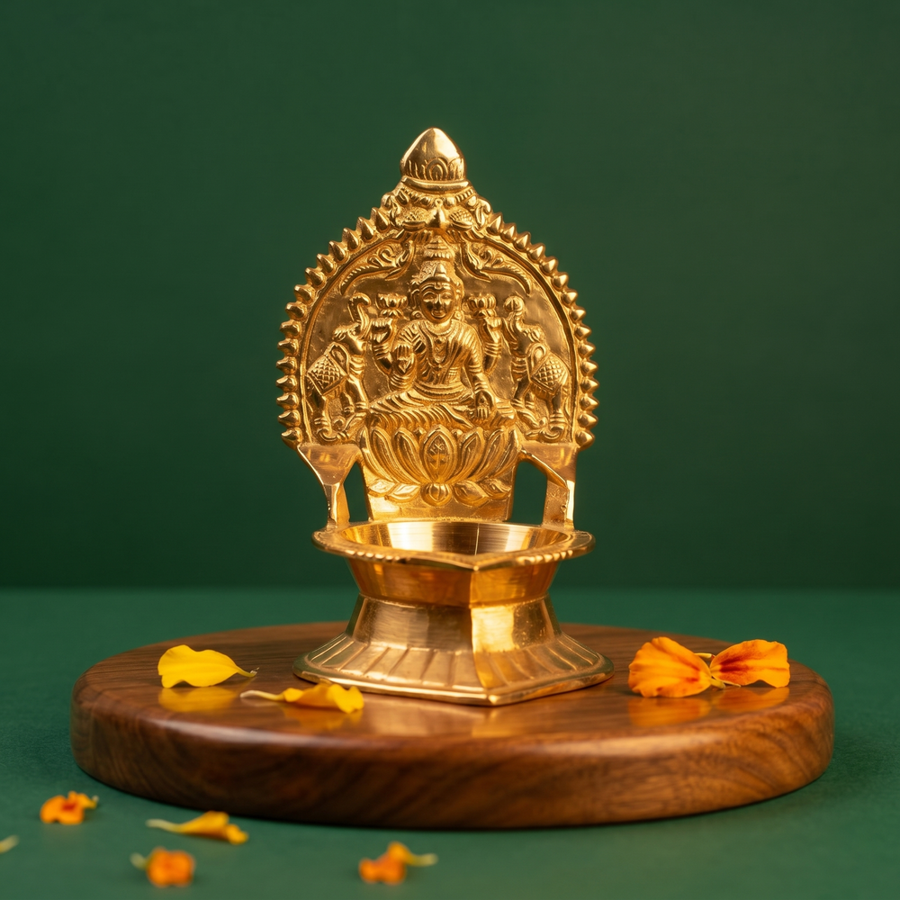 Kamakshi Deepam Vilakku with goddess on lotus and prabhavali in a slight left-angle view on a wooden base with petals against a green backdrop