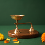 Brass Dhoopakal in right side angle with bell handle and deep bowl with yellow and orange marigolds on wooden plate.