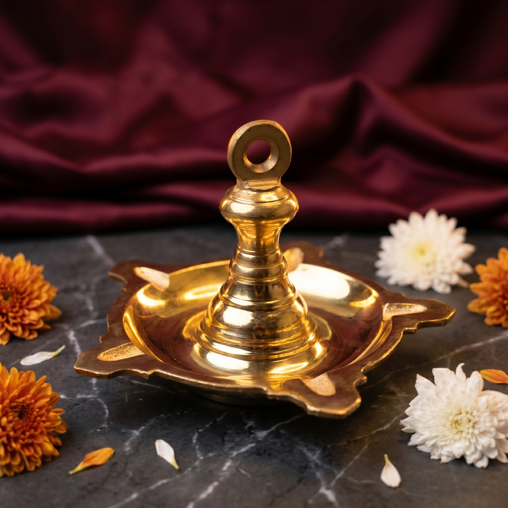 Thookku Vilakku with ring hook and scalloped base in a slight top-angle view on marble with white and orange flowers against a maroon backdrop