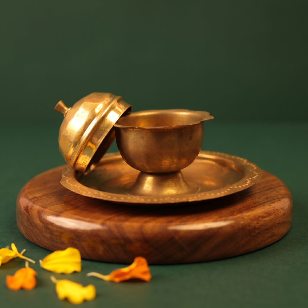 Brass Kumkum Sindoor Box shown open with lid beside it on a brass plate in a slight top-angle view on a wooden base against a green backdrop