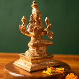 Lakshmi idol on the left side angle, seated with four arms on an engraved base with orange and yellow petals on a wooden plate.