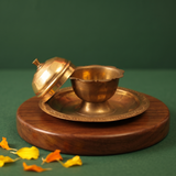 Brass Kumkum Sindoor Box open with scalloped inner bowl and domed lid kept aside in side-angle view on a wooden base against a green backdrop