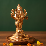 Ganesh Standing Valampuri on the left side angle with four arms and a mouse at base with scattered orange and yellow petals on a wooden plate.