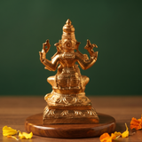 Ganesh Sitting Edampuri in back view, seated on a lotus base with four arms raised, with scattered yellow and orange petals on a wooden plate.