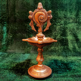 Fancy antique sangu vilaku straight front view with conch disc fish figures tall stem, square oil cup on round base, green backdrop