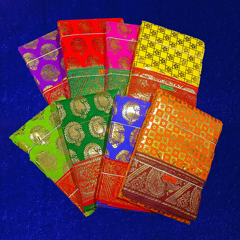 Eight folded Amman sarees in yellow, rose, red, maroon, dark green, light green, blue and dark yellow with gold zari design placed on blue velvet surface.