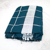 Bedsheet Meera folded in teal and white grid check cotton pattern with fringed edge on white surface, slight top-down angle view