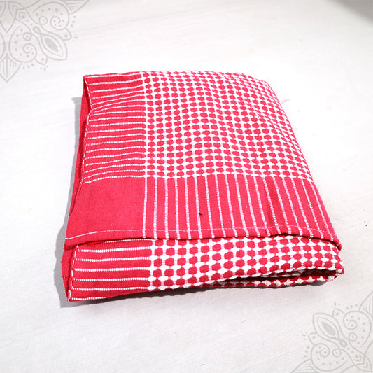 Bedsheet folded in red and white dot and stripe cotton pattern on white surface, slight top-down angle view