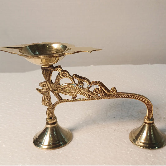 Eaga aarti small with peacock carved handle and twin bell feet, flower shaped diya bowl, slight left side angle view on white surface