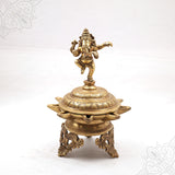 Fancy Vinayagar Vilakku with dancing Ganesha on top on engraved domed lamp with ornate stand in a straight front view against a white backdrop