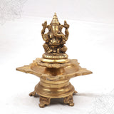 Fancy Vinayagar Vilakku with seated Ganesha on lotus on star-shaped lamp with decorative feet in straight front view against white backdrop
