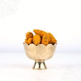 Raw manjal kizhangu turmeric roots filled in a scallop-edged puja bowl shown in closer front view against white backdrop.