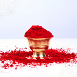 Red kumkum straight front view zoomed in with bright red sacred powder in golden ribbed bowl on pedestal with scattered kumkum around base