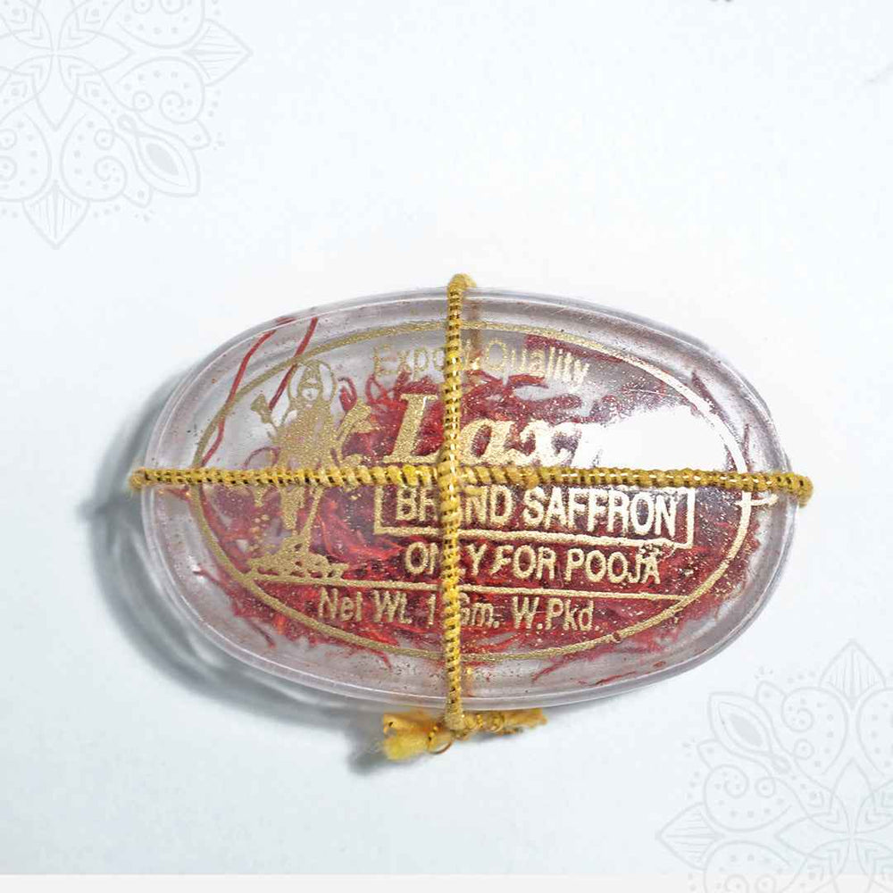 Laxmi brand saffron pooja oval clear box in a flat lay top-down view with gold thread tied across showing red saffron strands inside