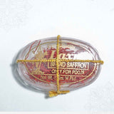 Laxmi brand saffron pooja oval clear box in a flat lay top-down view with gold thread tied across showing red saffron strands inside