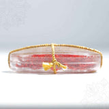 Saffron puja oval clear box in a straight front edge view showing gold thread tied across with red saffron strands visible inside