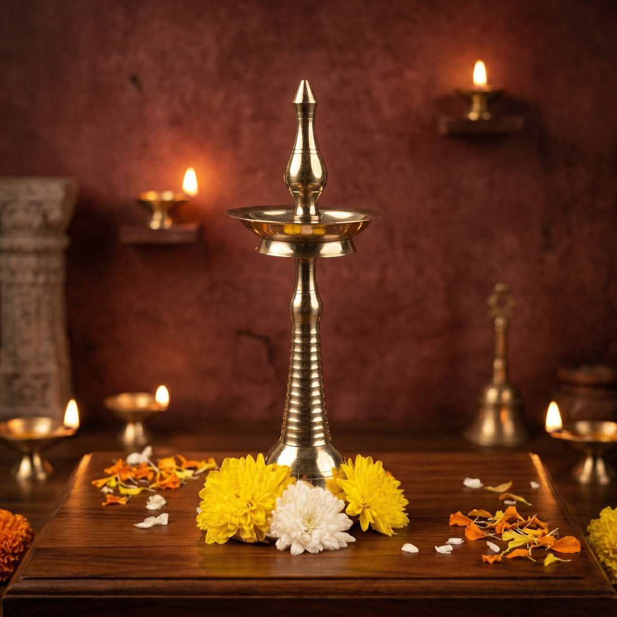 Nilavilakku Kerala floor lamp in front view with lit diyas and yellow white flowers on wooden surface against a maroon backdrop
