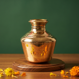 Brass Kalash Kodam in front view with tall polished round body and wide neck with yellow and orange marigolds on a wooden plate.