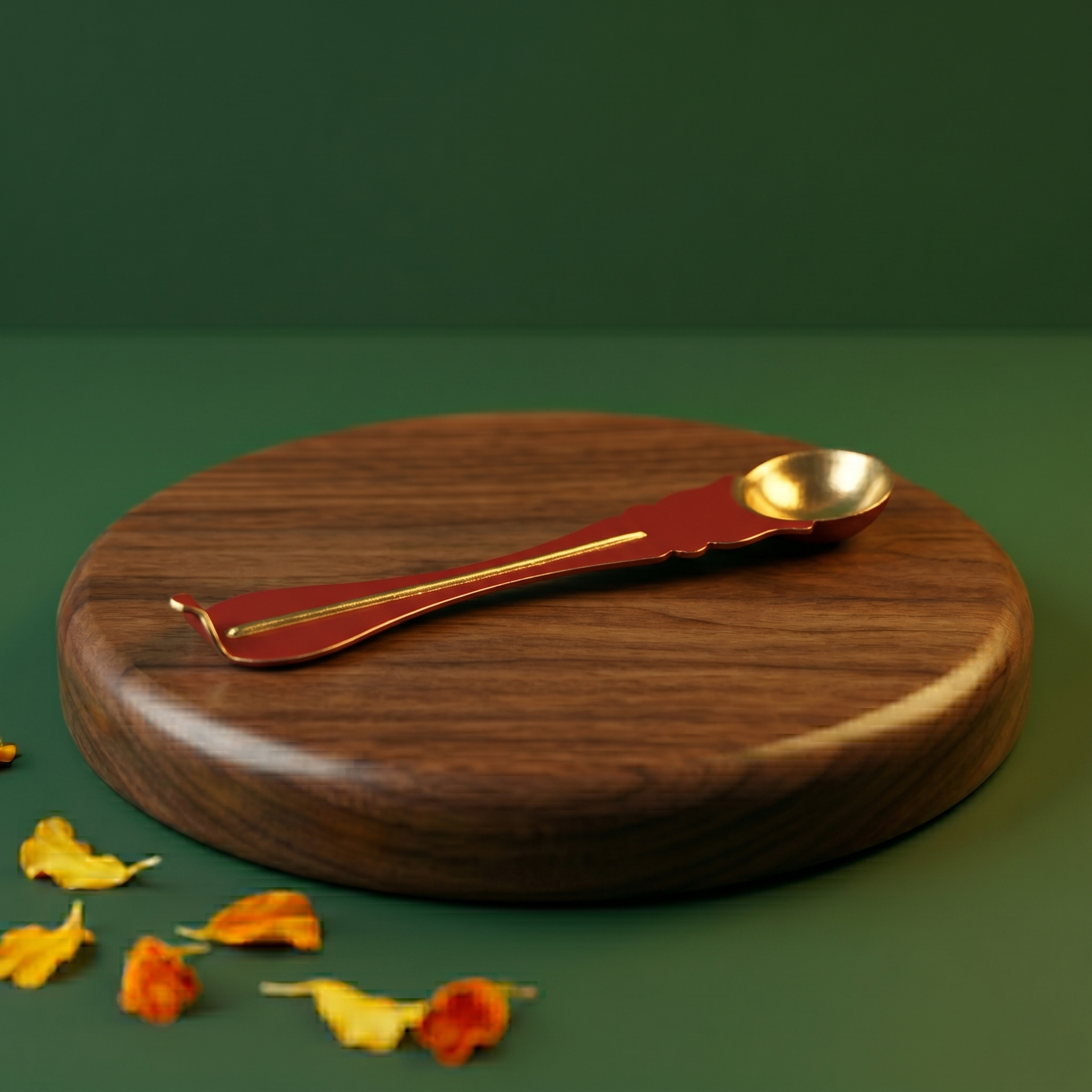 Brass Uthrani spoon with decorative handle on the left side angle on a wooden plate with scattered yellow and orange petals.