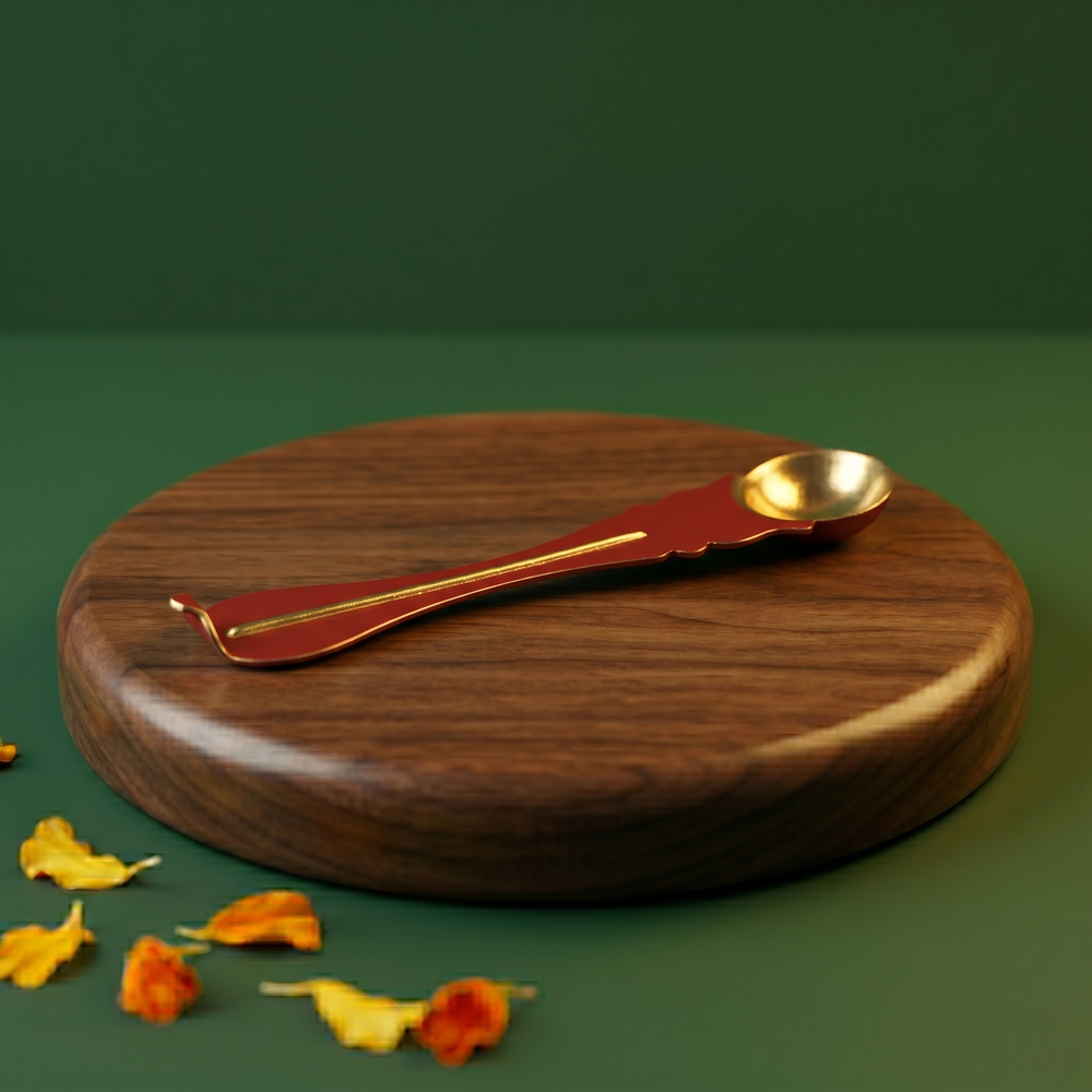 Brass Uthrani spoon with decorative handle on the left side angle on a wooden plate with scattered yellow and orange petals.