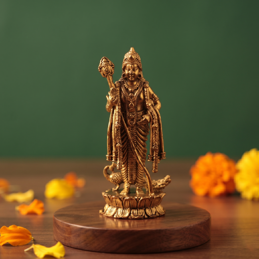 Brass Murugan statue in straight, front-facing view on a lotus base, holding a vel, on a wooden platform with marigold flowers, against a green backdrop.