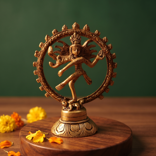 Brass Nataraja idol in a straight front-facing dancing pose within a fire ring, on a wooden platform with marigold flowers, green backdrop.
