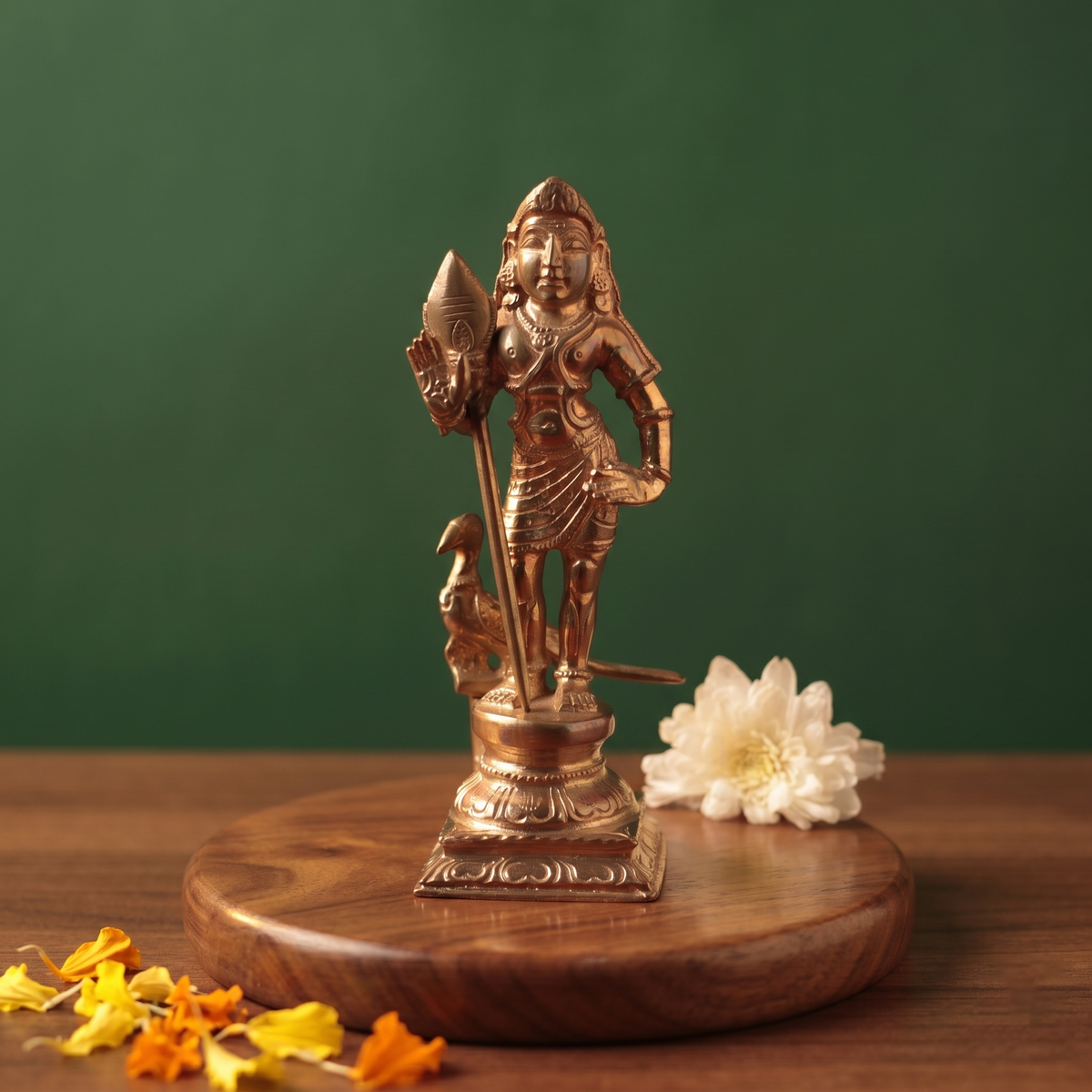 Bala Murugan with Peacock in front view holding vel with peacock at base with white flower and scattered petals on a wooden plate.