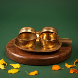 Two open brass Kumkum Sindoor Boxes with lids behind on a handled brass plate in a slight top-angle view on a wooden base against a green backdrop