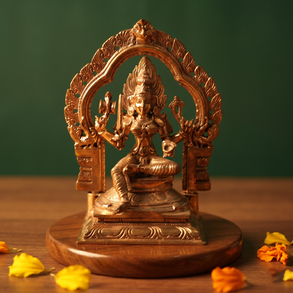 Maariamman idol in front view with decorative arch prabhavali seated on a lotus base with yellow and orange petals on a wooden plate.
