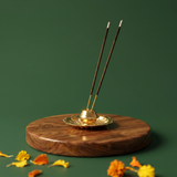 Brass Agarbatti Dhoop Stand in front view holding two incense sticks on a floral base with yellow and orange marigolds on a wooden plate.