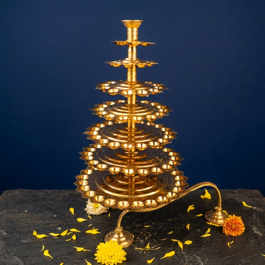Aal Vilakku Adukku Aarthi with tiered layers in a slight top-angle view with yellow and orange flowers on a stone surface against a blue backdrop