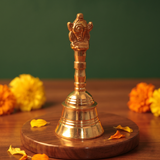 Brass Ghanti Bell Changuchakkaram in front view with Garuda handle and tiered bell base with yellow and orange marigolds on a wooden plate.