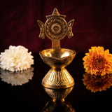 Sangu Chakaram Vilakku with floral chakra in front view with white and orange flowers on dark reflective surface against maroon backdrop