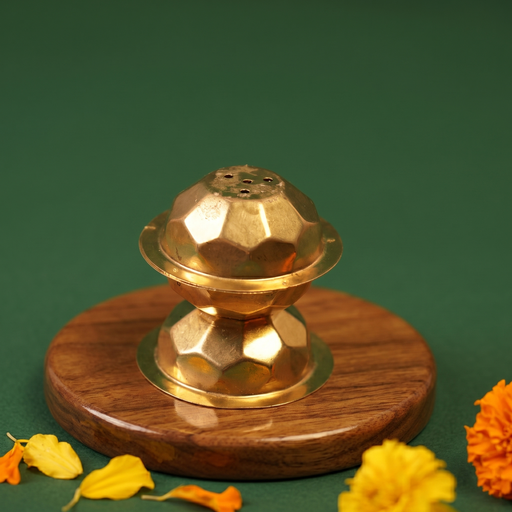Brass Agarbatti Dhoop Stand in a slight top angle with geometric ball shape and incense holes with yellow and orange marigolds on a wooden plate.