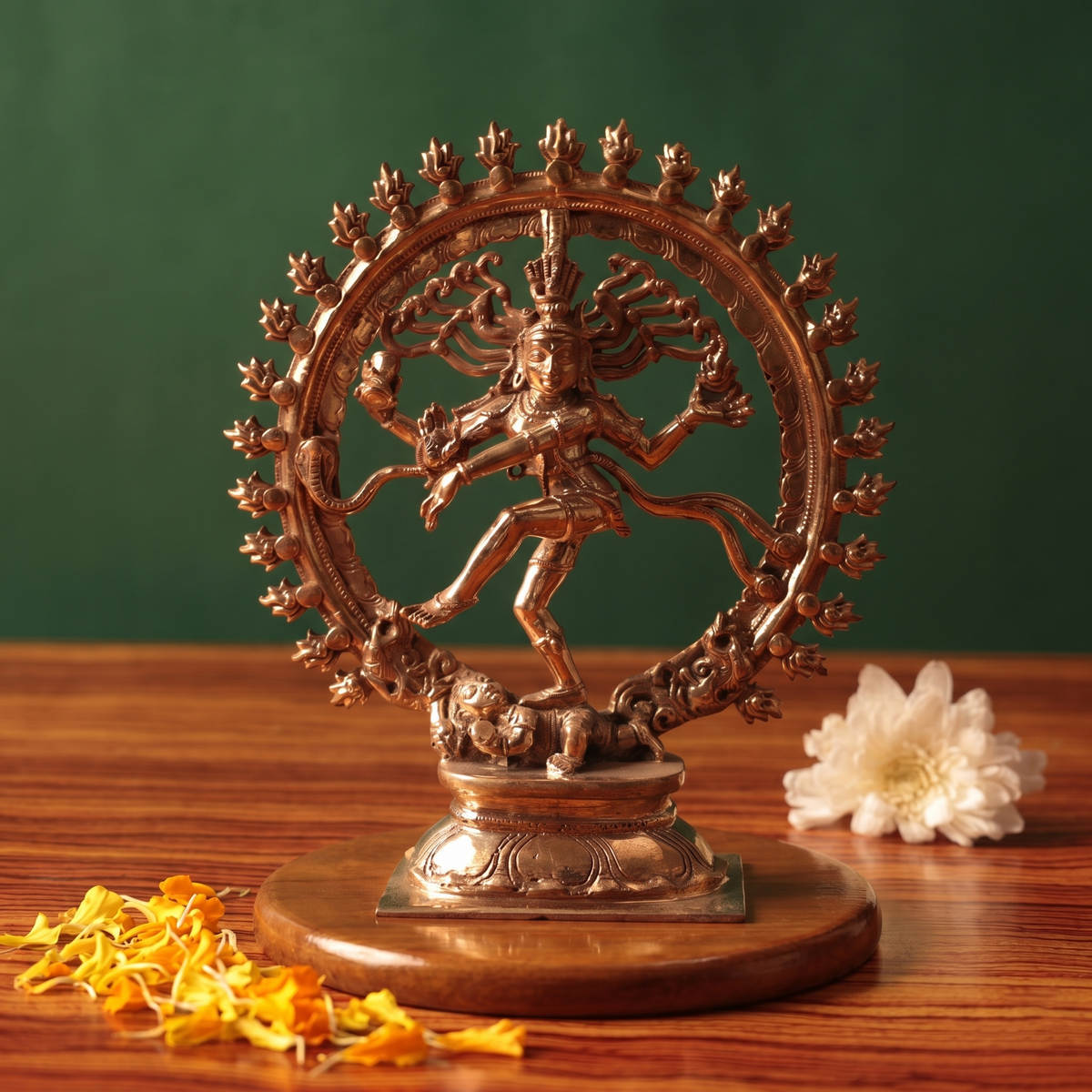 Nataraja idol in front view, dancing within a fire ring on a lotus base with white flowers and scattered petals on a wooden plate.